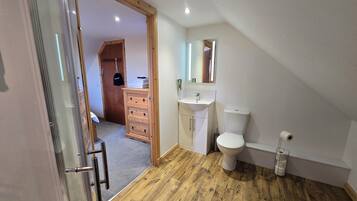A modern bathroom with a wooden floor, a white sink, a toilet, and a glass shower enclosure.