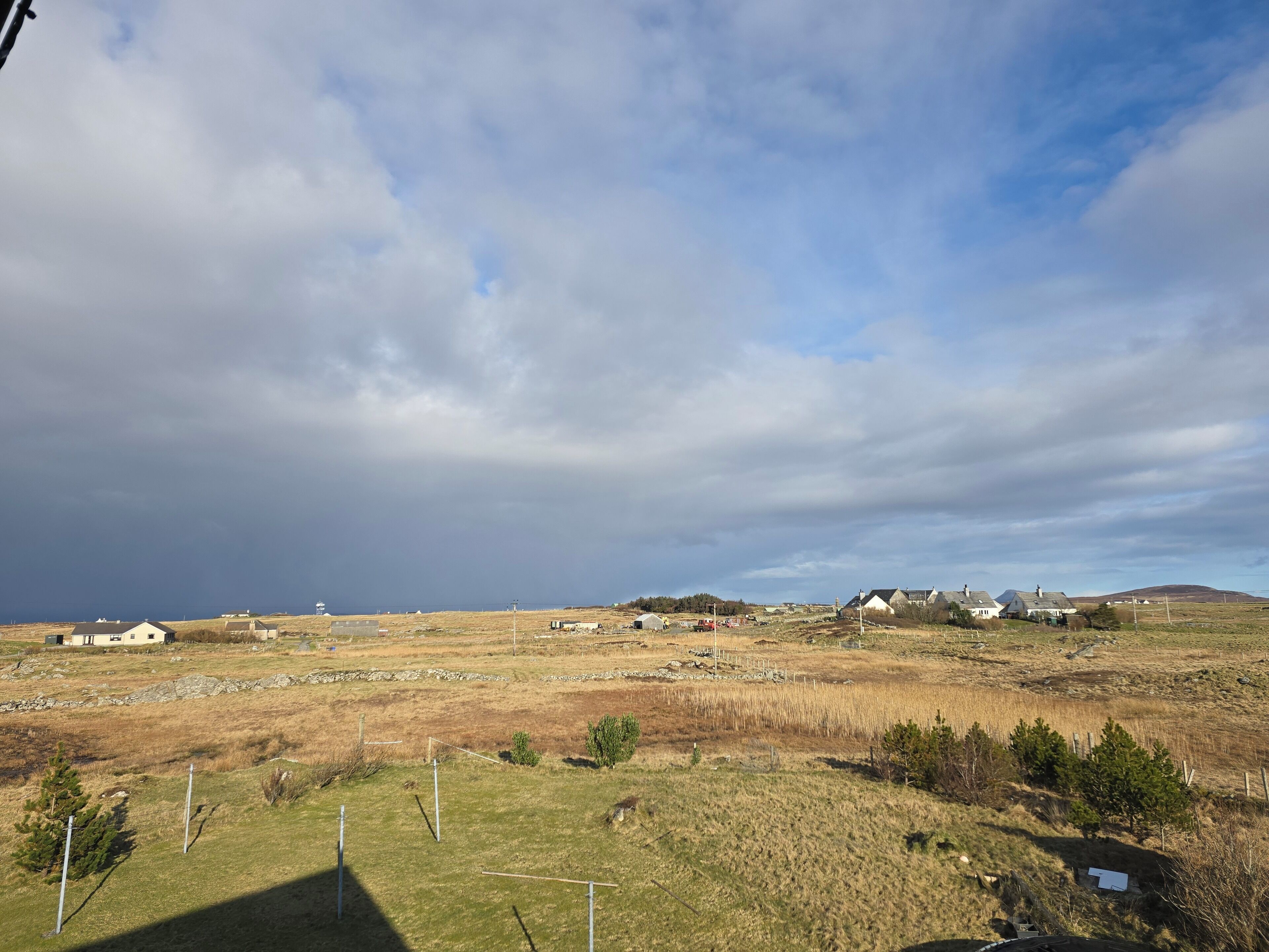Un paysage rural avec des maisons, des champs à perte de vue et un ciel nuageux.