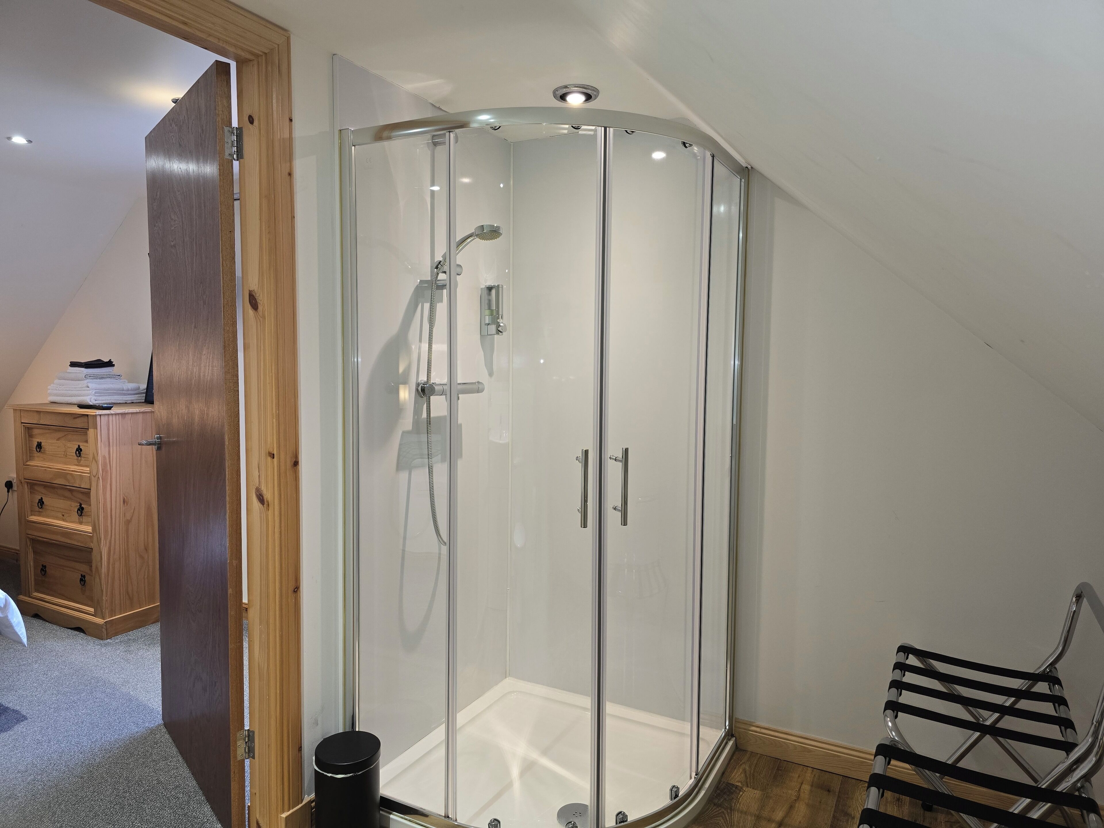 Eine Eckdusche mit Glastüren, ein Holzschrank und ein Stuhl.