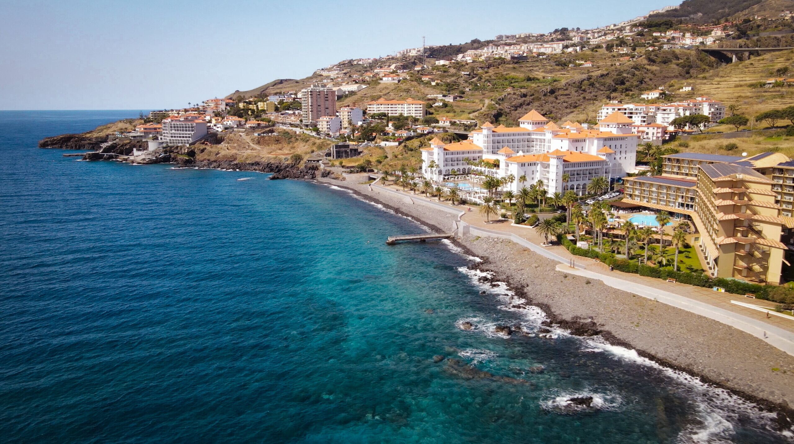 Un hôtel situé sur la côte, composé de plusieurs bâtiments, avec une plage et un pont.