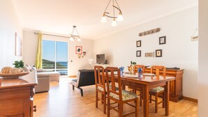 A spacious living area with a dining table, wooden chairs, a sofa, and a TV. - Sunrising Apartment by Atlantic Holiday (Santa Cruz)