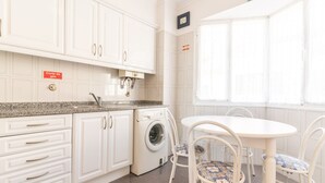 A kitchen with white cabinets, a washing machine, and a dining table with chairs. - Sunrising Apartment by Atlantic Holiday (Santa Cruz)