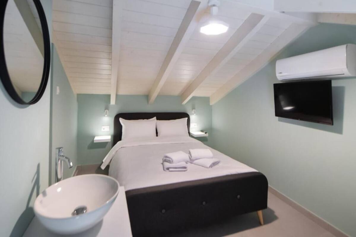 Une chambre à coucher comprenant un lit, un lavabo rond blanc, un miroir, un téléviseur à écran plat et un appareil de climatisation.