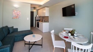 A modern living room with a sofa, a round table, and a dining area with chairs and a TV mounted on the wall. - Dawn Apartments (Lefkada)