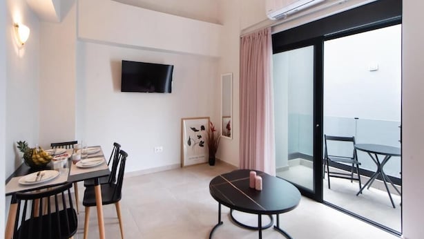 A modern room with a dining area, a small round table, and a balcony with outdoor seating. - Dawn Apartments (Lefkada)