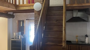 Een houten trap die leidt naar een hoger gelegen deel met een rode gordijn en een fotolijst aan de wand.