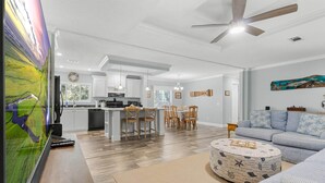 A spacious living area with a large flat-screen TV, a ceiling fan, and a dining area with wooden chairs and a table. - Fin & Feather - Steinhatchee Florida (Steinhatchee)