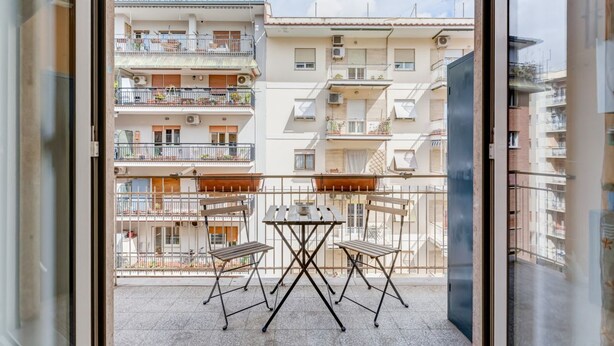 Un balcon avec une table et des chaises, une vue sur des immeubles à étages multiples et un ciel dégagé.