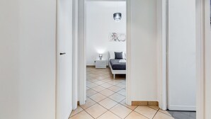 Un couloir menant à une chambre à coucher équipée d’un lit, d’une table de chevet et d’un luminaire suspendu.