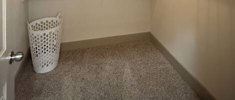 Un armario pequeño con alfombra, tres estantes de madera y un cesto blanco para ropa.