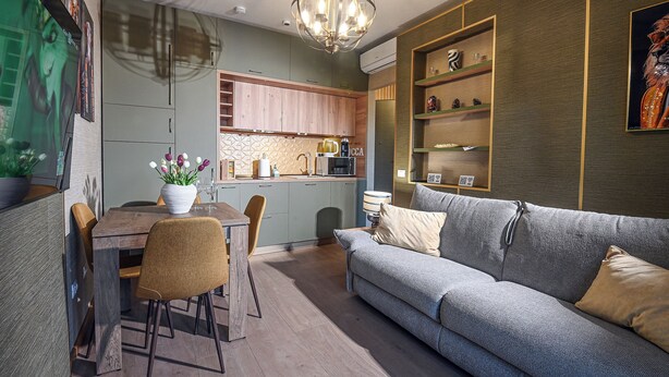 A modern living room with a grey sofa, wooden dining table, and chairs. A chandelier hangs from the ceiling, and there is a kitchen area visible in the background. - Accogliente appartamento situato a Olbia,
A 2 km dall'aeroporto.. (Olbia)