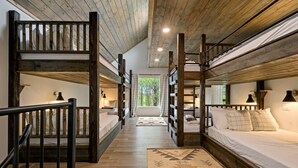 A multi-level wooden bunk bed room with a central walkway, wooden beams, and a view of greenery outside. - 5 Bedroom Sleeps 24 , Pets OK, Hot Tub, Game Room. (Broken Bow)