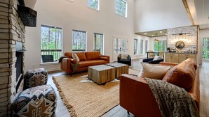 A spacious living room with a fireplace, large windows, and a cozy seating area. - 5 Bedroom Sleeps 24 , Pets OK, Hot Tub, Game Room. (Broken Bow)