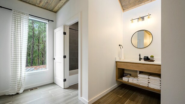 A bathroom with a wooden vanity, a round mirror, and a shelf with towels. - 5 Bedroom Sleeps 24 , Pets OK, Hot Tub, Game Room. (Broken Bow)