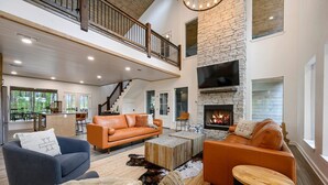 A spacious living area with a fireplace, leather sofas, and a high ceiling with exposed beams. - 5 Bedroom Sleeps 24 , Pets OK, Hot Tub, Game Room. (Broken Bow)