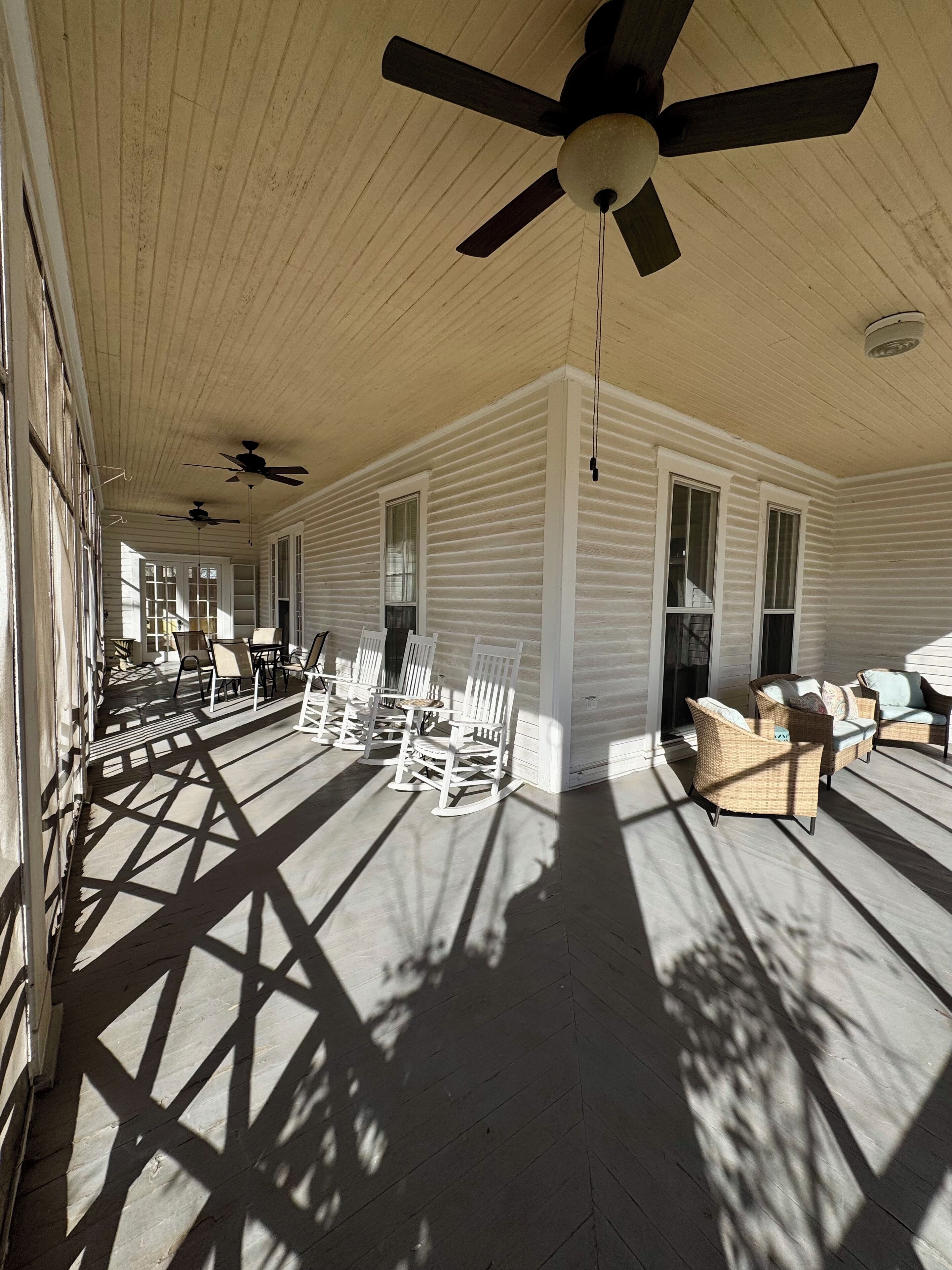 A covered porch with ceiling fans, rocking chairs, and wicker furniture.