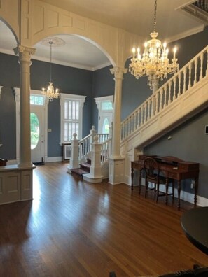 Una habitación amplia con una imponente escalera, suelo de madera y elegantes candelabros.