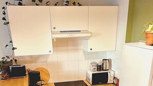 Een compacte keuken met witte kastjes, een ingebouwde oven, een magnetron en een spoelbak.