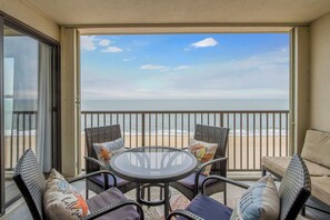 A balcony with wicker furniture, a glass table, and a view of the beach. - Sandpiper Dunes 1009 (Ocean City)