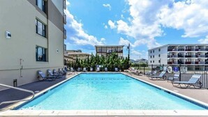 A swimming pool with lounge chairs, surrounded by buildings and a clear sky. - Sandpiper Dunes 1009 (Ocean City)