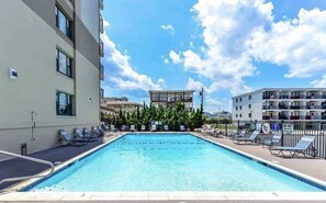 Ein Pool mit Liegestühlen, umgeben von Gebäuden und blauem Himmel.