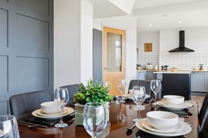A modern dining area with a wooden table set for six, surrounded by grey upholstered chairs. A potted plant adds a touch of greenery. - Spacious 4B home, great for families/contractors (Greater Manchester)