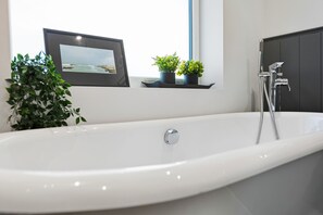 A modern bathroom with a white bathtub, a framed picture on the wall, and two potted plants on a windowsill. - Spacious 4B home, great for families/contractors (Greater Manchester)