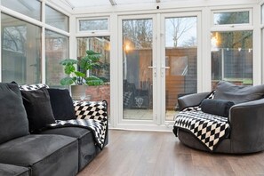 A conservatory with a glass door, a grey sofa, and a checkered throw blanket. - 4 Bed 8 Guest Home With 2 Car Private Parking (Greater Manchester)