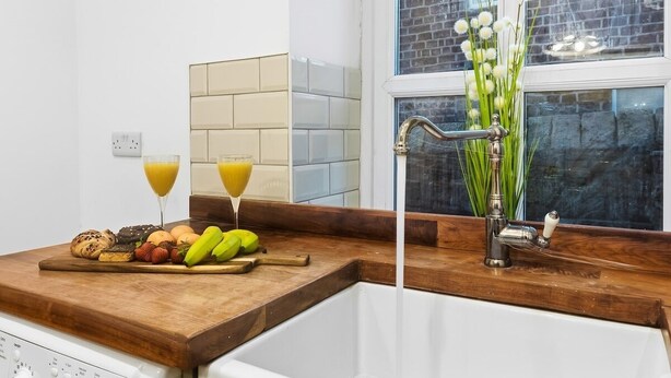 A kitchen with a wooden countertop, a sink, and a window with a view of a brick building. - Beautiful Country Cottage with Views! - Sleeps 8 (Holcombe)