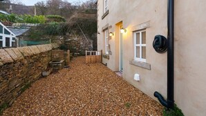 A stone wall, a gravel courtyard, and a building with a door and windows. - Beautiful Country Cottage with Views! - Sleeps 8 (Holcombe)