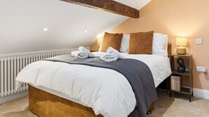A bedroom with a large bed, a wooden ceiling beam, a white radiator, a bedside table with a lamp, and a bookshelf. - Beautiful Country Cottage with Views! - Sleeps 8 (Holcombe)