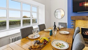 A dining area with a wooden table set for four, a fireplace, and a television on the wall. - Beautiful Country Cottage with Views! - Sleeps 8 (Holcombe)