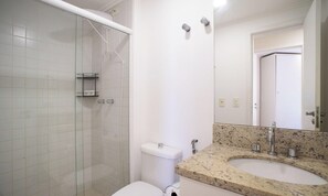 A bathroom with a glass shower enclosure, a toilet, a sink with a granite countertop, and a mirror. - Beachfront Condominium w/ Pool in Morro das Pedras - Pros (Florianópolis)