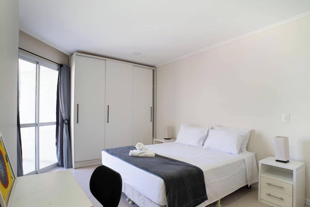 A hotel room with a bed, bedside tables, a desk, and a wardrobe.