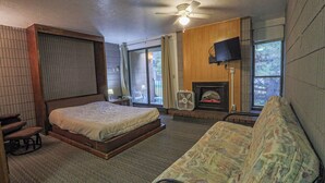 Ein Schlafzimmer mit Bett, Sofa, Kamin, Deckenventilator und Wandfernseher.