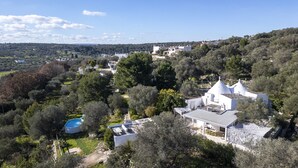 Una proprietà su una collina con piscina, edifici bianchi e vegetazione rigogliosa.
