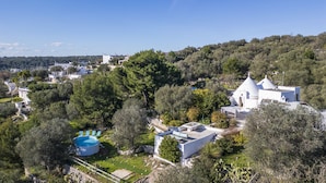 Un edificio bianco con una cupola, circondato da alberi e una piscina.
