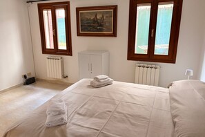 A bedroom with a bed, two windows, a radiator, a cabinet, and a painting on the wall. - Beach holiday at Venice Lido: comfort and charm in Art Nouveau style (Venezia)