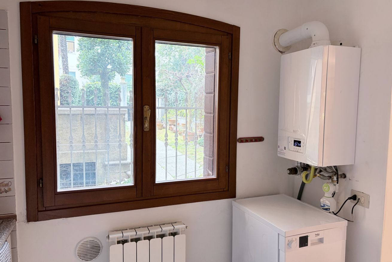 A room with a radiator, a white heater, and a window with a wooden frame.