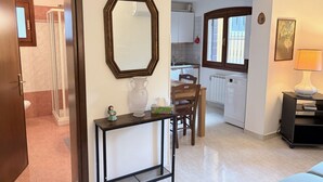 Eine moderne Küche mit weißen Schränken, einem Esstisch und Stühlen. An der Wand hängt ein großer Spiegel und auf dem Tisch steht eine Vase.