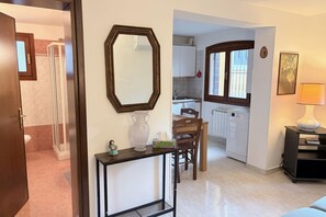 A modern kitchen with white cabinets, a dining table, and chairs. There is a large mirror on the wall and a vase on the table. - Beach holiday at Venice Lido: comfort and charm in Art Nouveau style (Venezia)