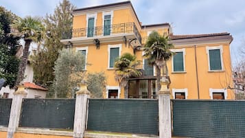 A two-story building with a balcony, surrounded by a green fence and palm trees.