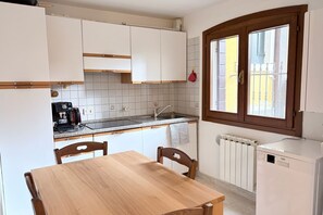 A compact kitchen with white cabinets, a wooden table, and a window with a view of a yellow building. - Beach holiday at Venice Lido: comfort and charm in Art Nouveau style (Venezia)
