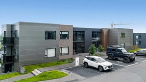 Um edifício moderno com telhado plano, grandes janelas e um estacionamento com carros e um caminhão.