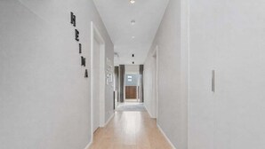 Corredor moderno com paredes em tons claros e soalho de madeira, que dá acesso a um quarto com porta.
