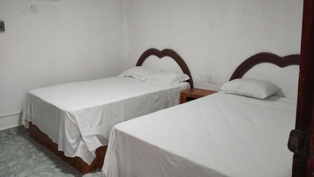 Two single beds with wooden headboards in a room with white walls and a marble floor. - Kom Shot 38 (Cancún)