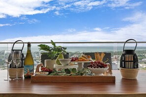 A table with a bottle of wine, a bowl of grapes, and a tray of snacks with a scenic view in the background. - Sunset Dreaming Skyline and Harbour Vista with Pool (Darwin)