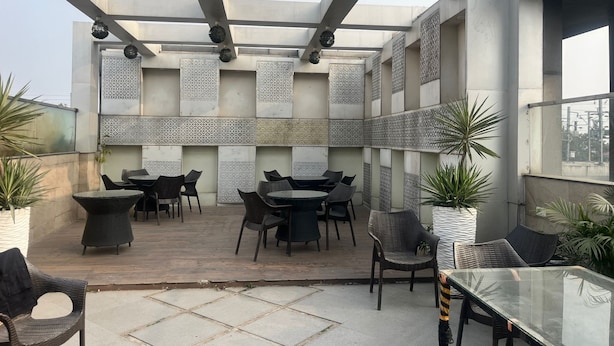 An outdoor patio area with tables and chairs, decorative panels, and potted plants. - Staylo Masterprice Palace (Lucknow)