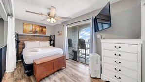 A modern bedroom with a bed, a ceiling fan, a TV, and a sliding glass door to a balcony. - Cozy Beach Retreat Near Whitecap & Padre Island (Corpus Christi)