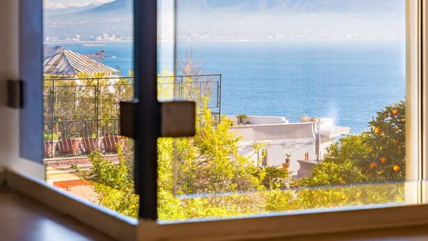Una habitación con un ventanal que ofrece vistas a una montaña, el mar y un paisaje urbano.